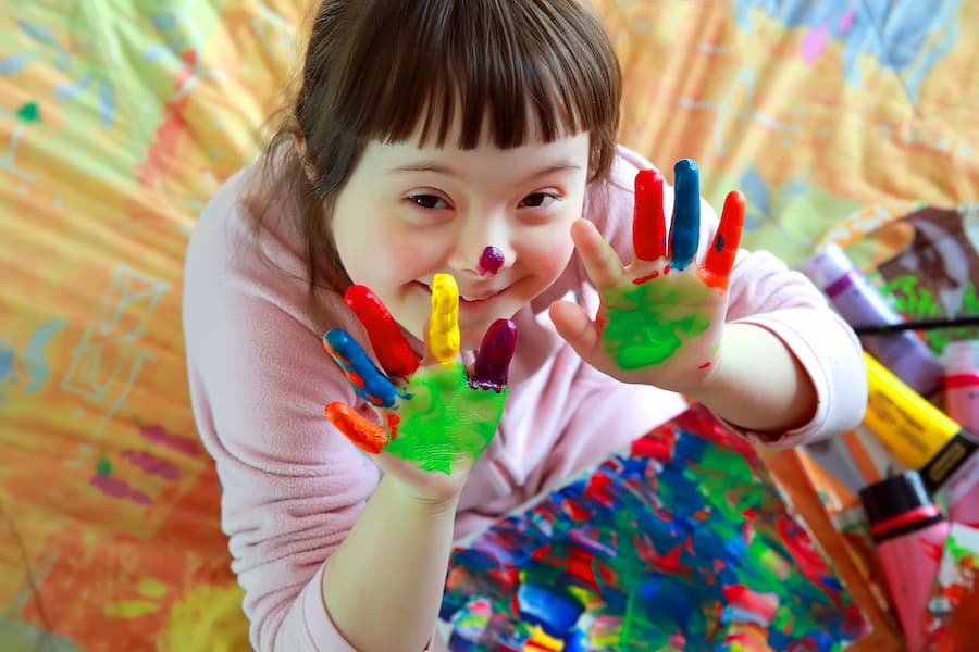 Smiling child with painted hands showing bright rainbow colors, engaged in a joyful art activity.