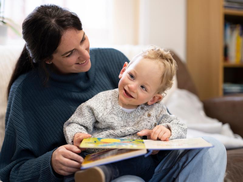 Smiling mother reading a picture book with her toddler at home.