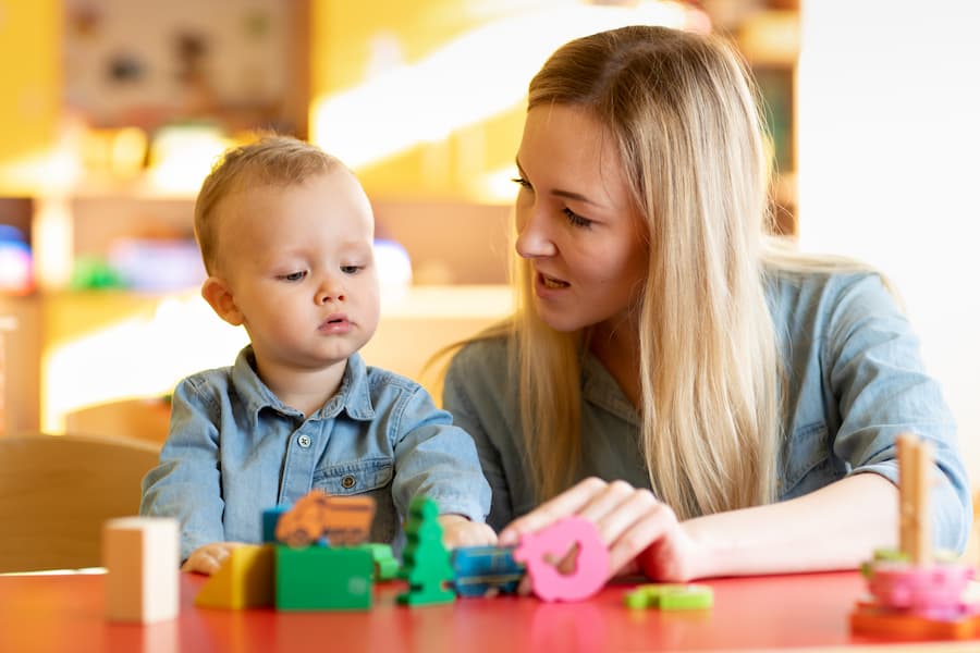 Teacher helping a young child build with colorful wooden toys at a table.